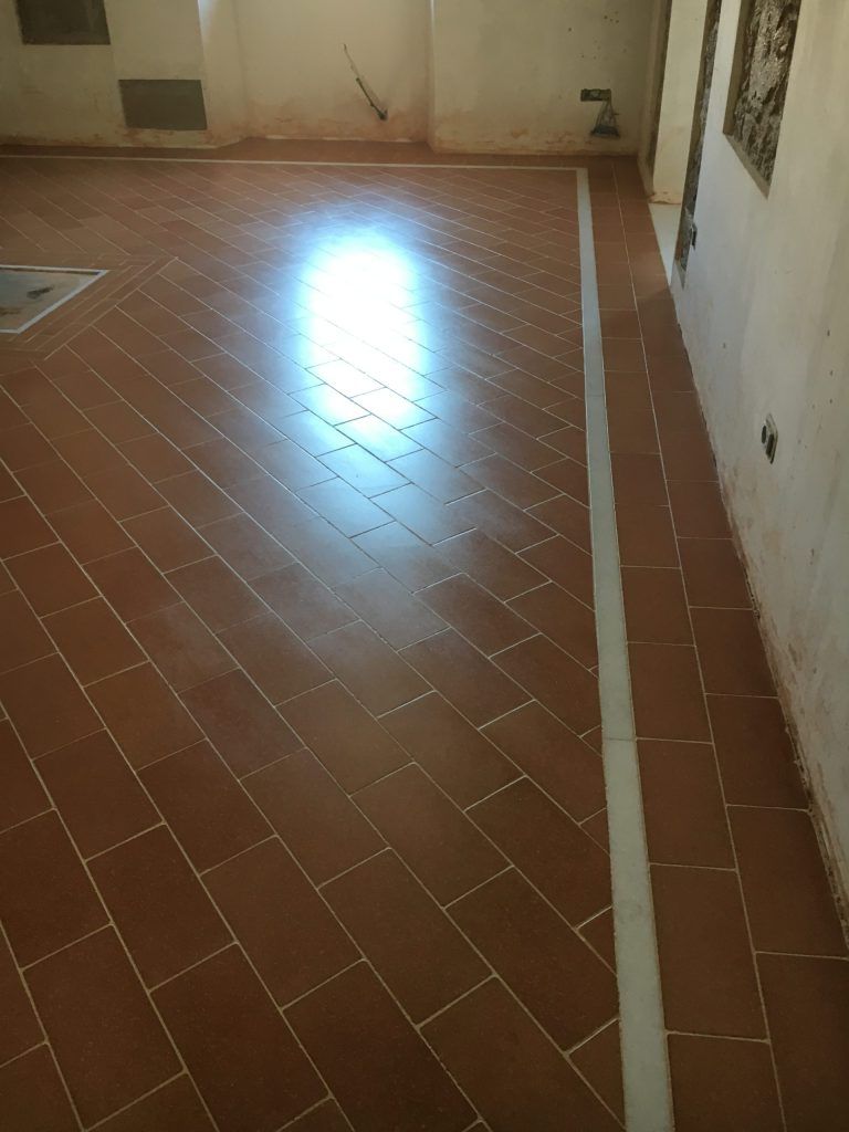 Stanza vuota piastrellata con una zona illuminata dal sole sul pavimento e una lunga striscia bianca lungo il lato destro.