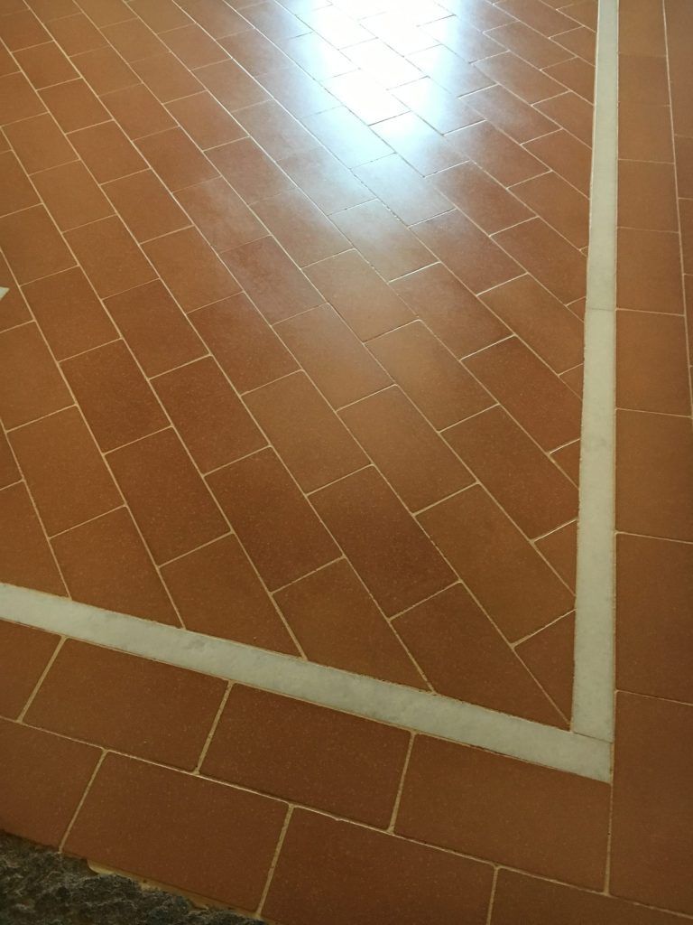 Pavimento piastrellato marrone con finiture bianche e un brillante riflesso di luce sulla superficie.