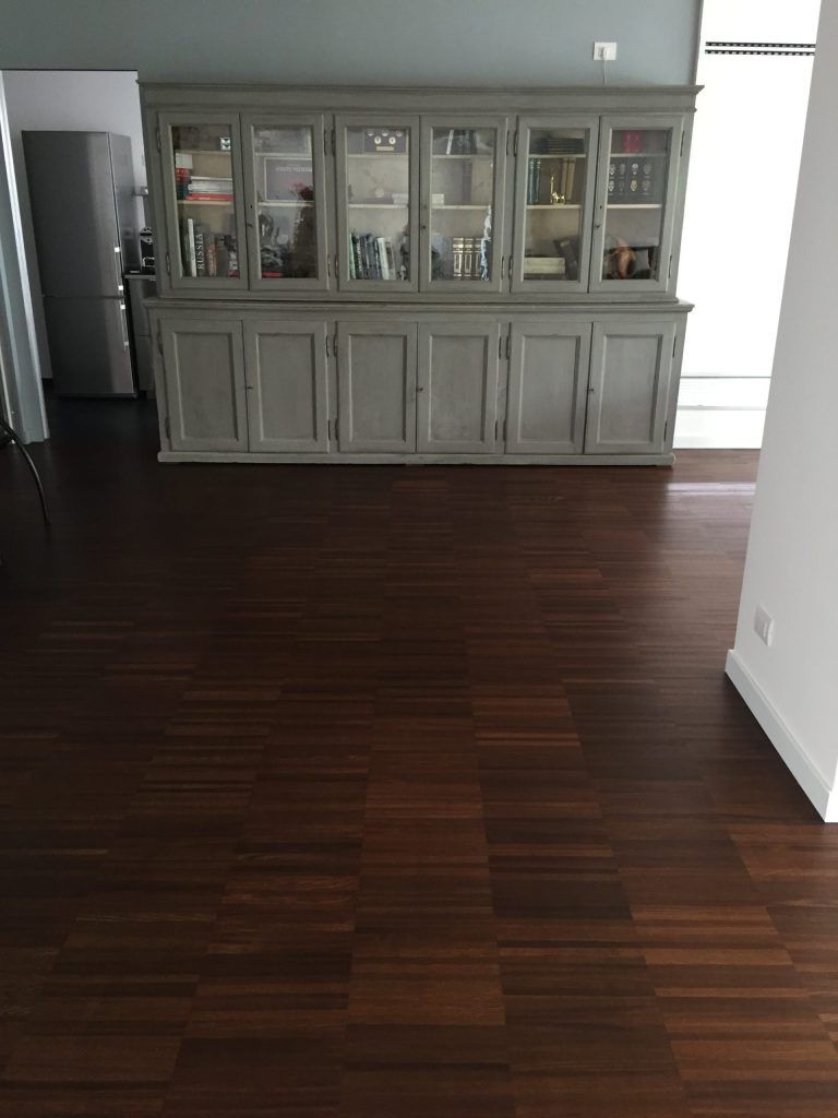 Soggiorno vuoto con pavimento in legno scuro e un grande mobile grigio con ante in vetro contro la parete di fondo.