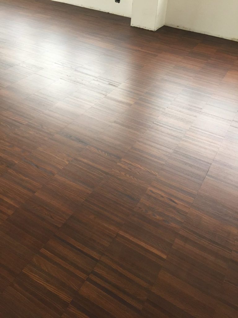 Stanza vuota con pavimento in legno scuro e battiscopa bianchi, illuminata da luce naturale.