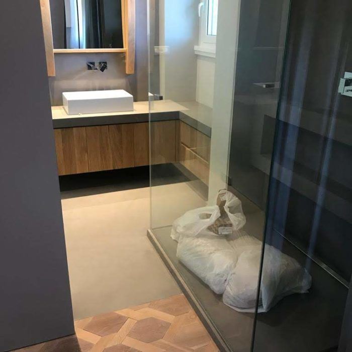 Bagno moderno con mobile lavabo, box doccia in vetro e asciugamano o borsa bianca sul pavimento della doccia.