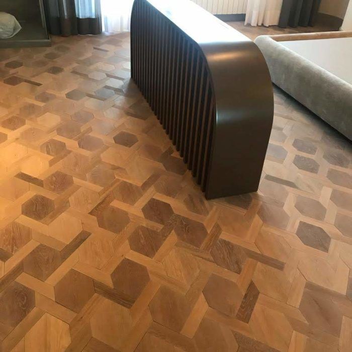 Stanza moderna con pavimento in legno a motivi geometrici e una parete divisoria curva scura tra il divano e le tende.