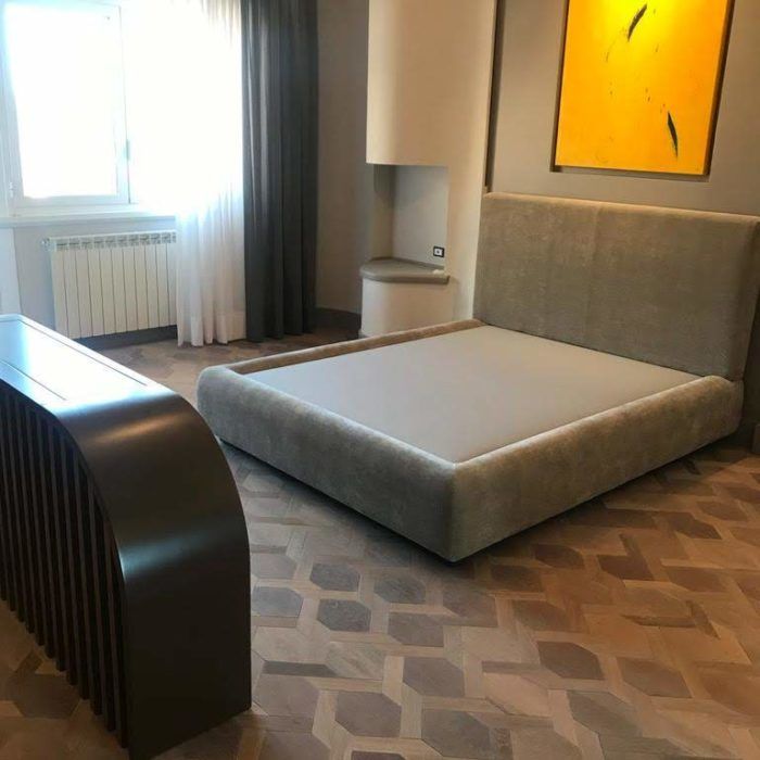 Camera da letto moderna con letto basso grigio, moquette a motivi geometrici, finestra e quadro astratto alla parete.