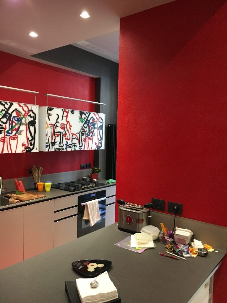 Cucina moderna con pareti rosse, isola scura e colorati quadri astratti sopra il lavello.