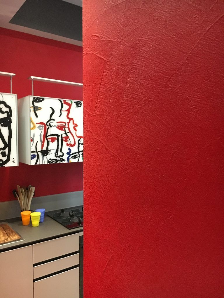 Parete rossa dello studio accanto a un bancone con materiali artistici e dipinti astratti.