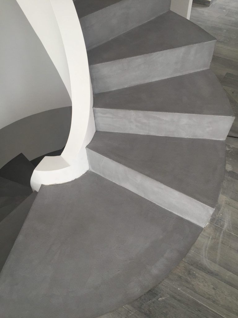 Scala curva grigia con ringhiera bianca in un interno moderno.