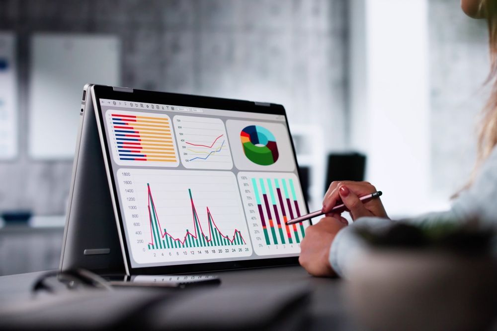 Laptop showing colorful business charts while a person points with a pen