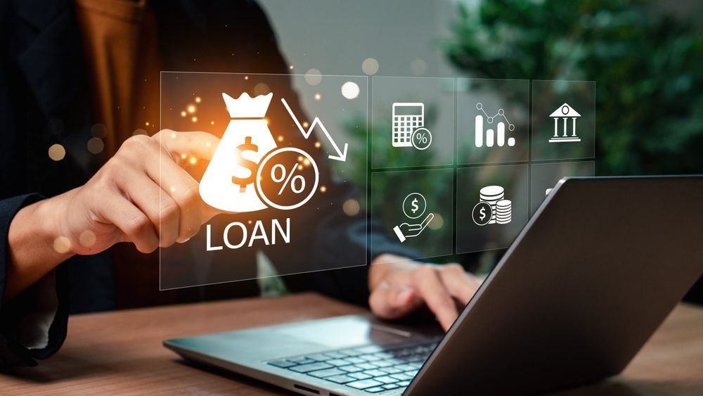 Person interacting with loan graphic on laptop. Icons of finance surround a loan bag.