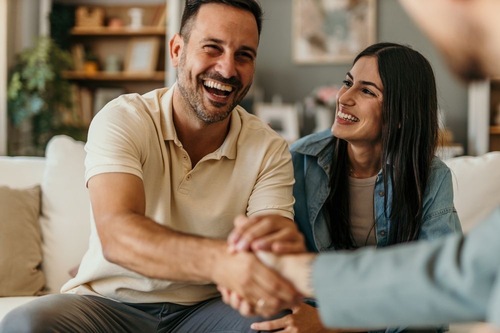 Smiling couple shaking hands with another person indoors.