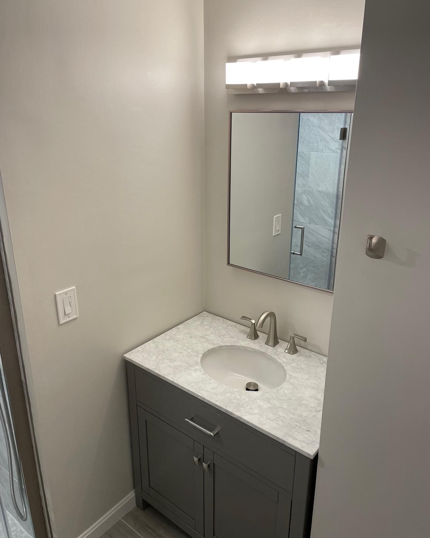 A grey bathroom vanity with a white speckled countertop, a silver faucet, and a rectangular mirror under a wall light.