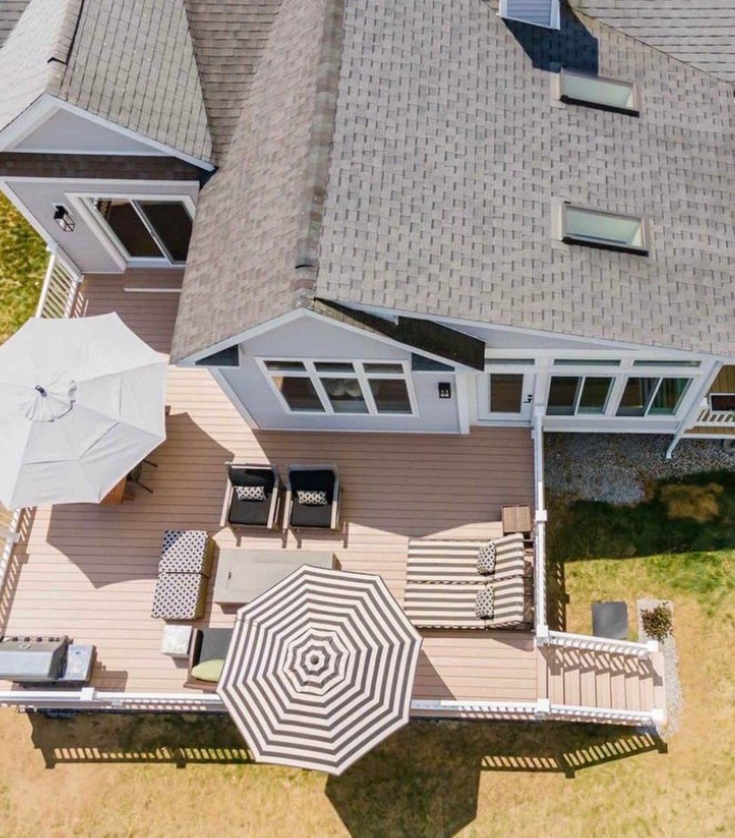 Aerial view of a residential deck featuring lounge chairs, a cushioned bench, outdoor umbrellas, and a grill.