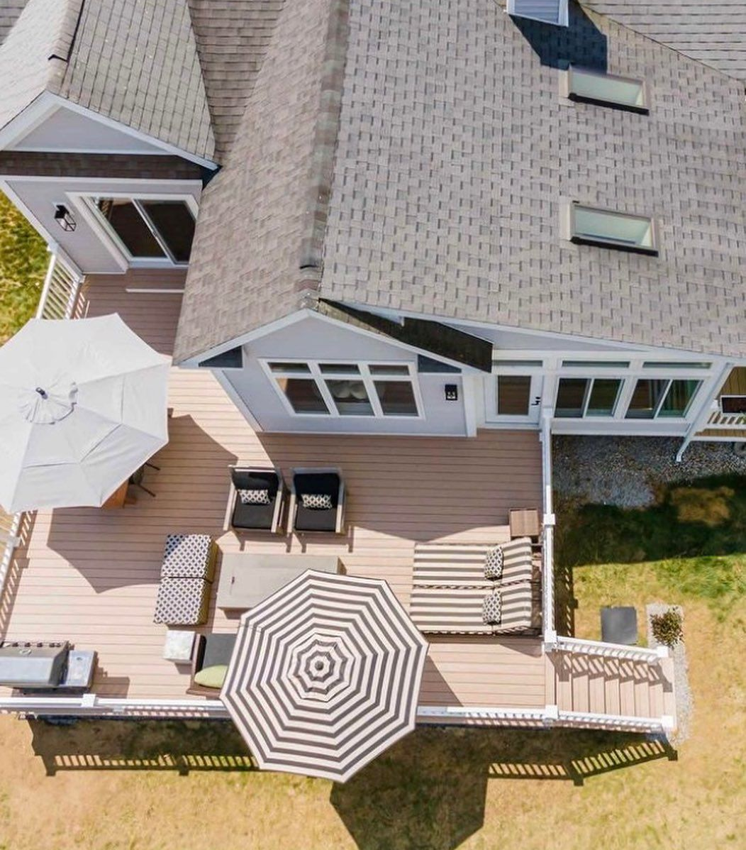 Aerial view of a house deck featuring outdoor furniture, two umbrellas, and a set of stairs leading to the yard.