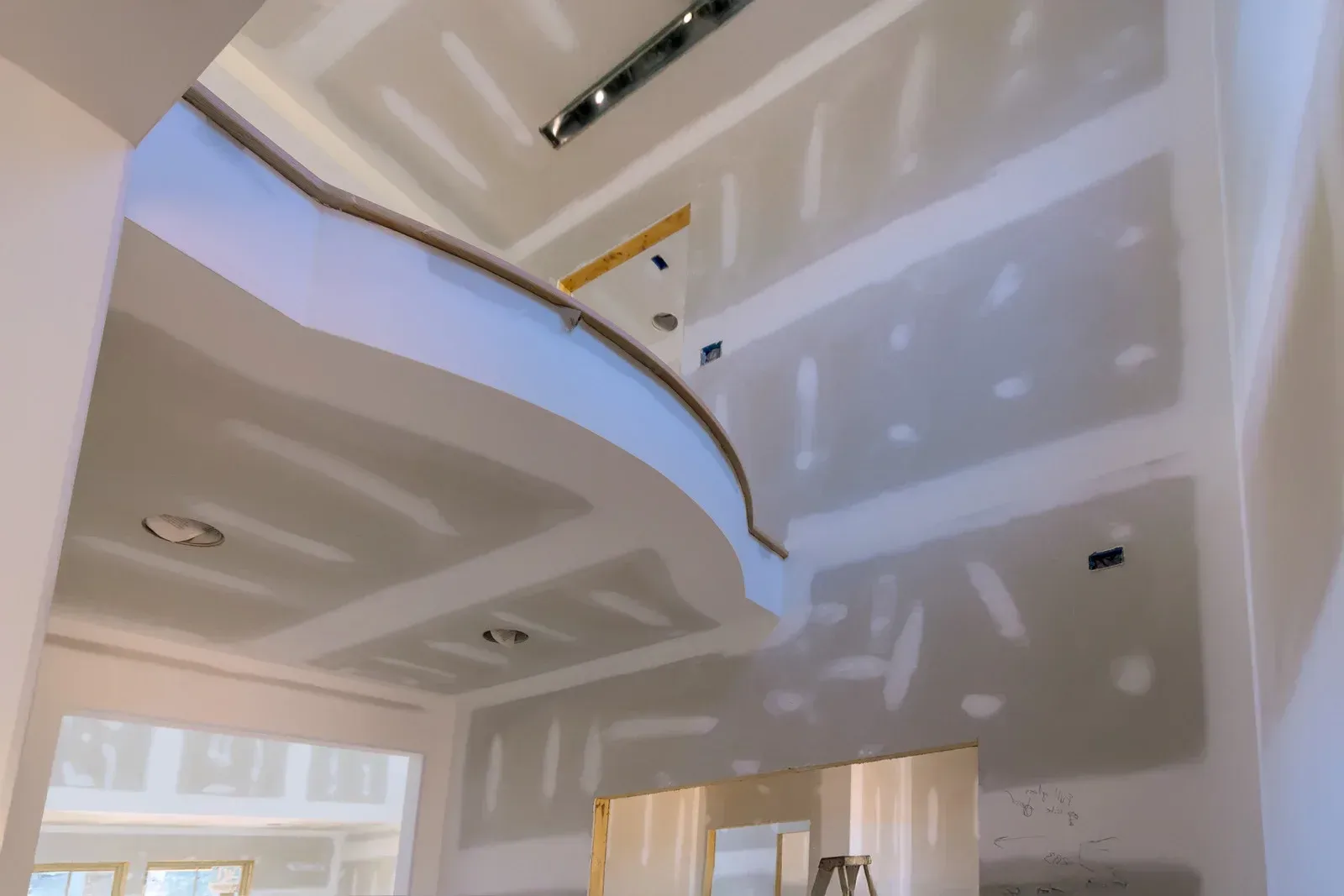 Interior view of a residential room under construction featuring unfinished drywall, mudded seams, and a curved ceiling.
