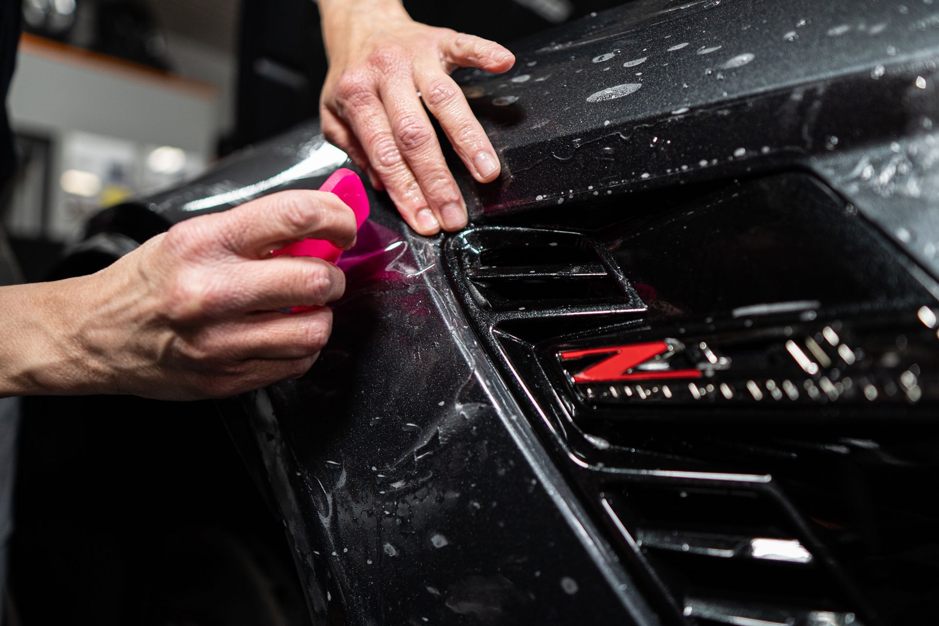 A person is applying a protective film to a black car.