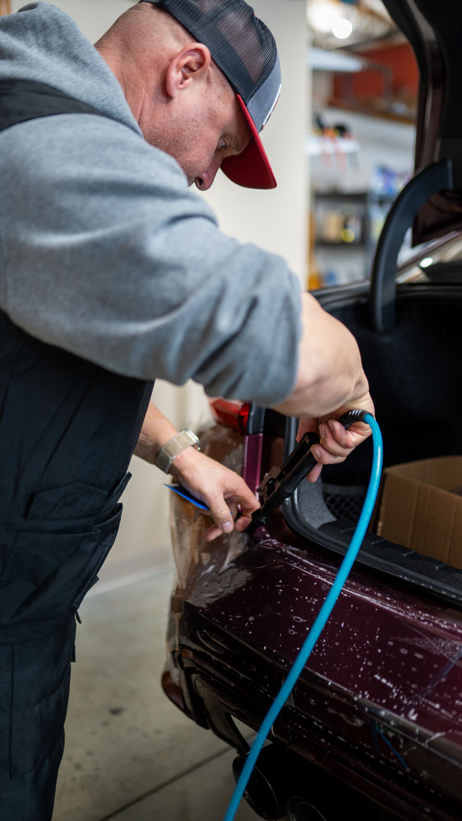 A man is working on the back of a car with a hose.
