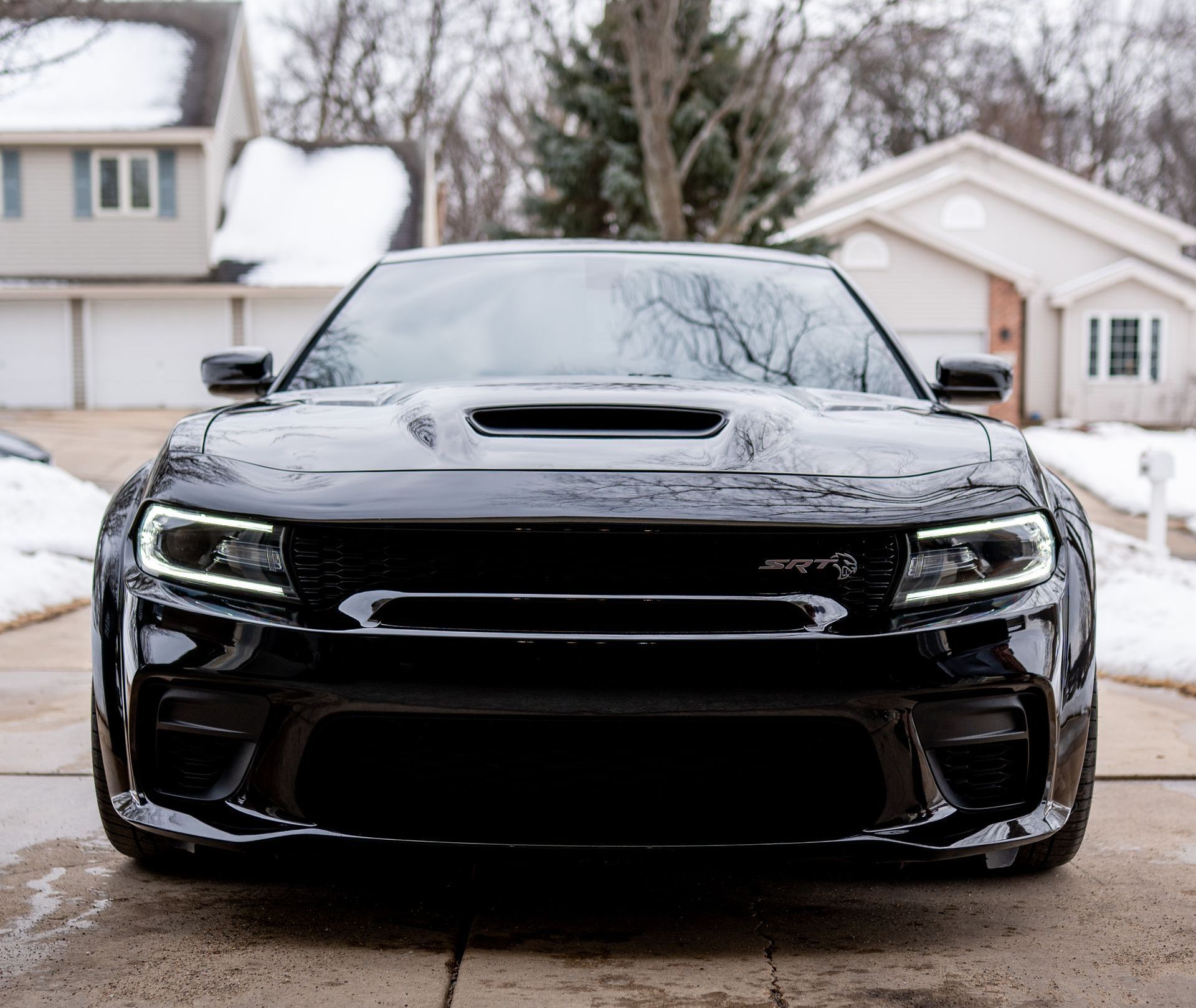 Black Dodge Charger SRT Hellcat parked in front of a house, snowy setting.
