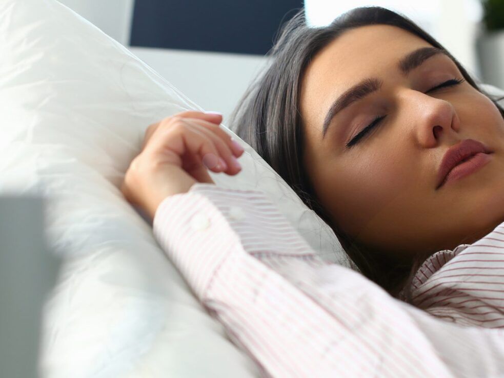 A woman is sleeping on a bed with her eyes closed.