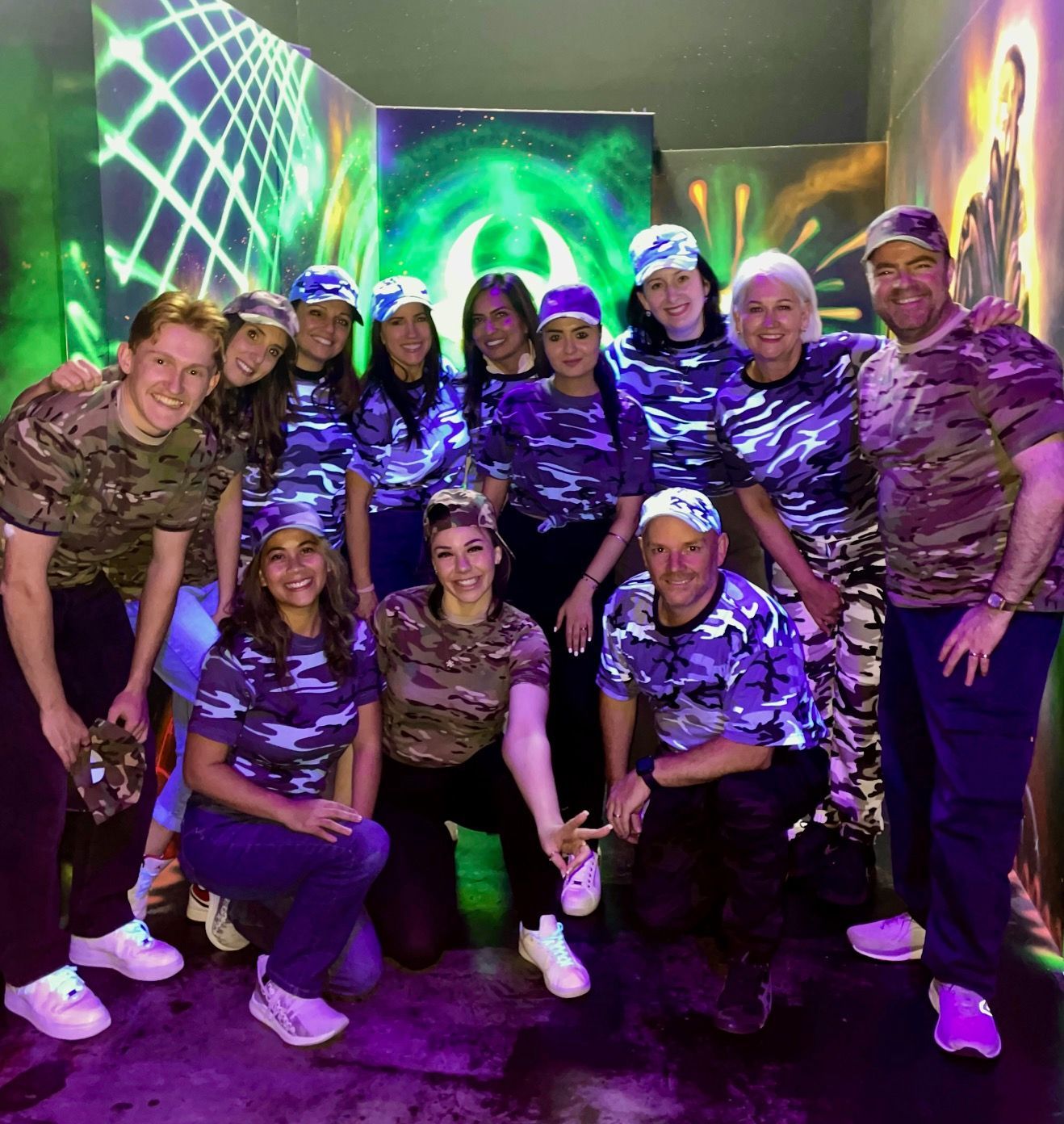 Group in matching purple shirts posing in a neon-lit room with green and purple glowing walls