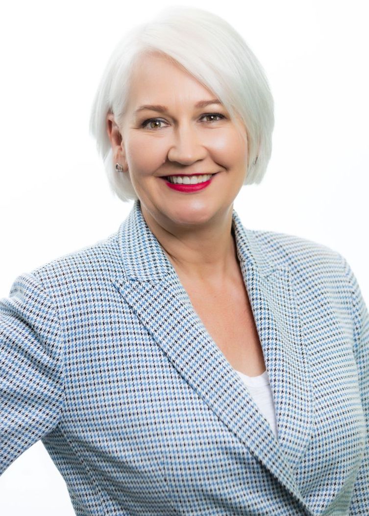 Smiling woman with short white hair in a light blue patterned blazer against a white background