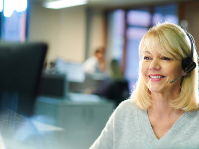 A woman wearing a headset is smiling while sitting in front of a computer.