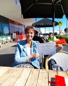 A woman is sitting at a table holding a certificate.