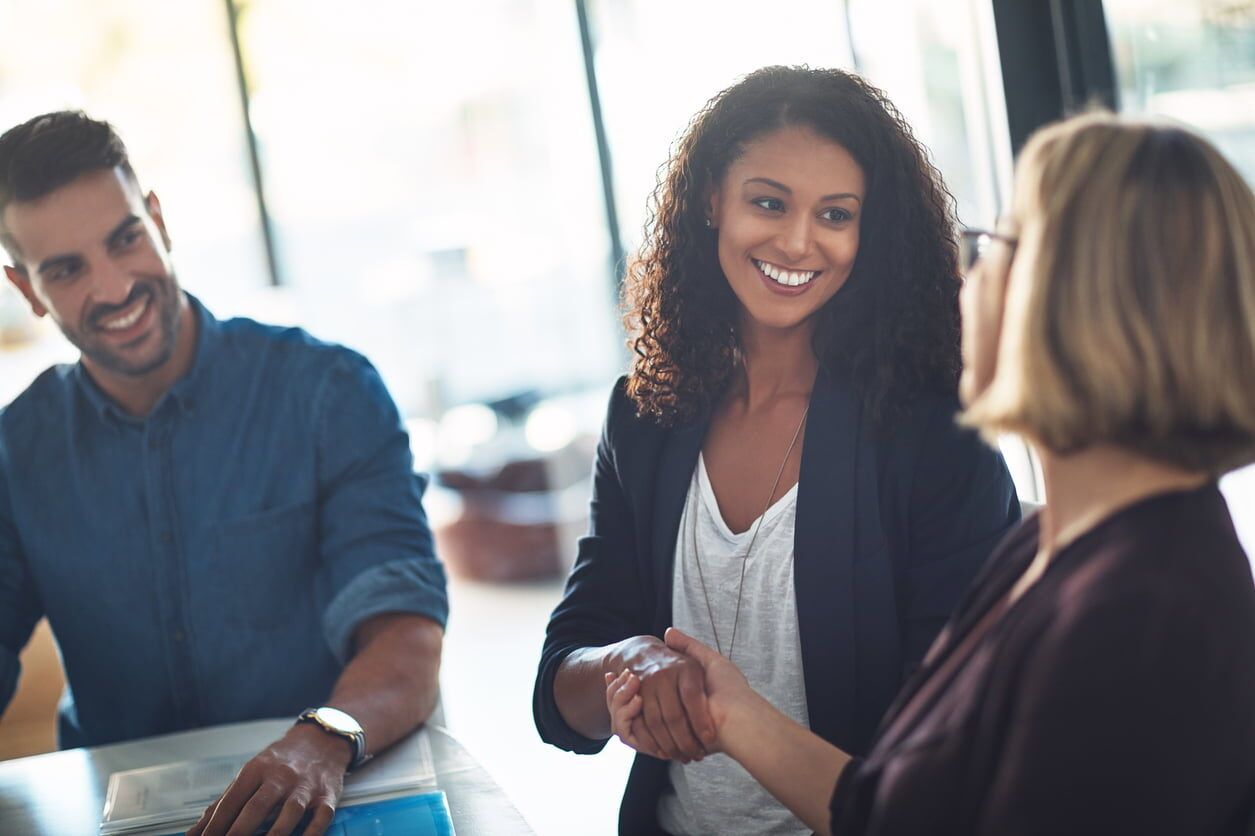 Three coworkers smiling and talking in a bright office meeting room