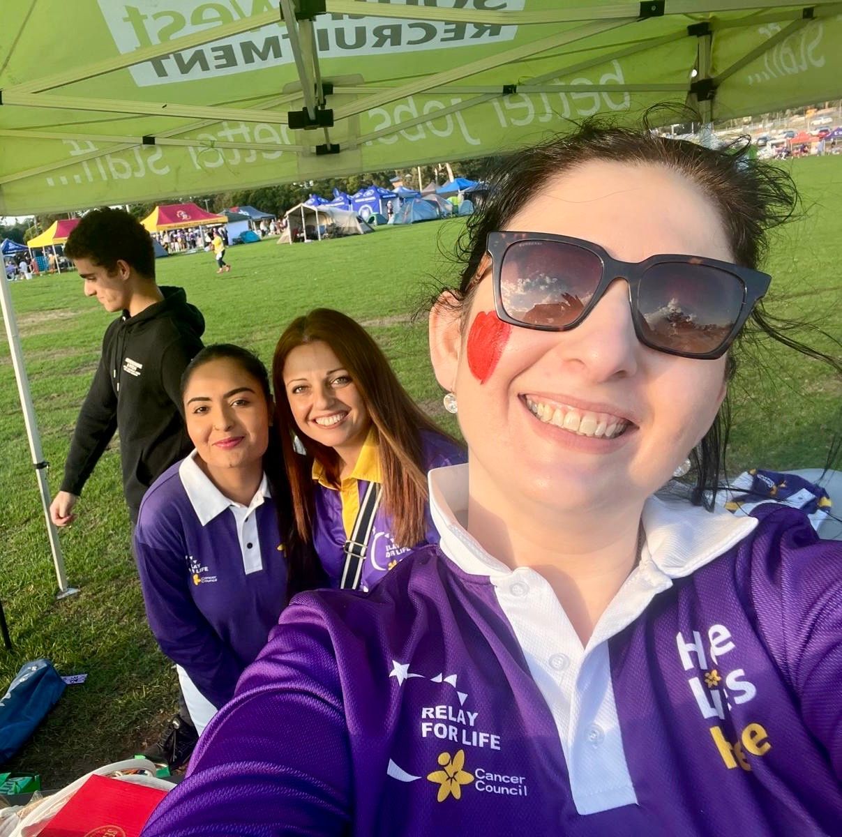 Four smiling people in purple shirts at an outdoor event under a green tent