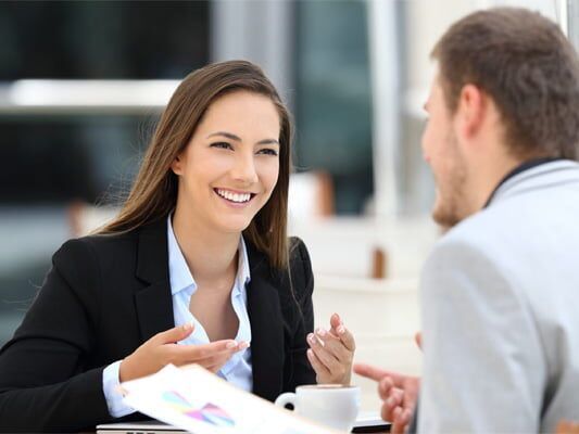 A woman is sitting at a table talking to a man.