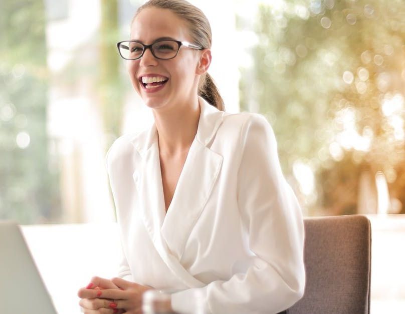 Smiling woman in glasses and white blouse seated at a table in a bright office