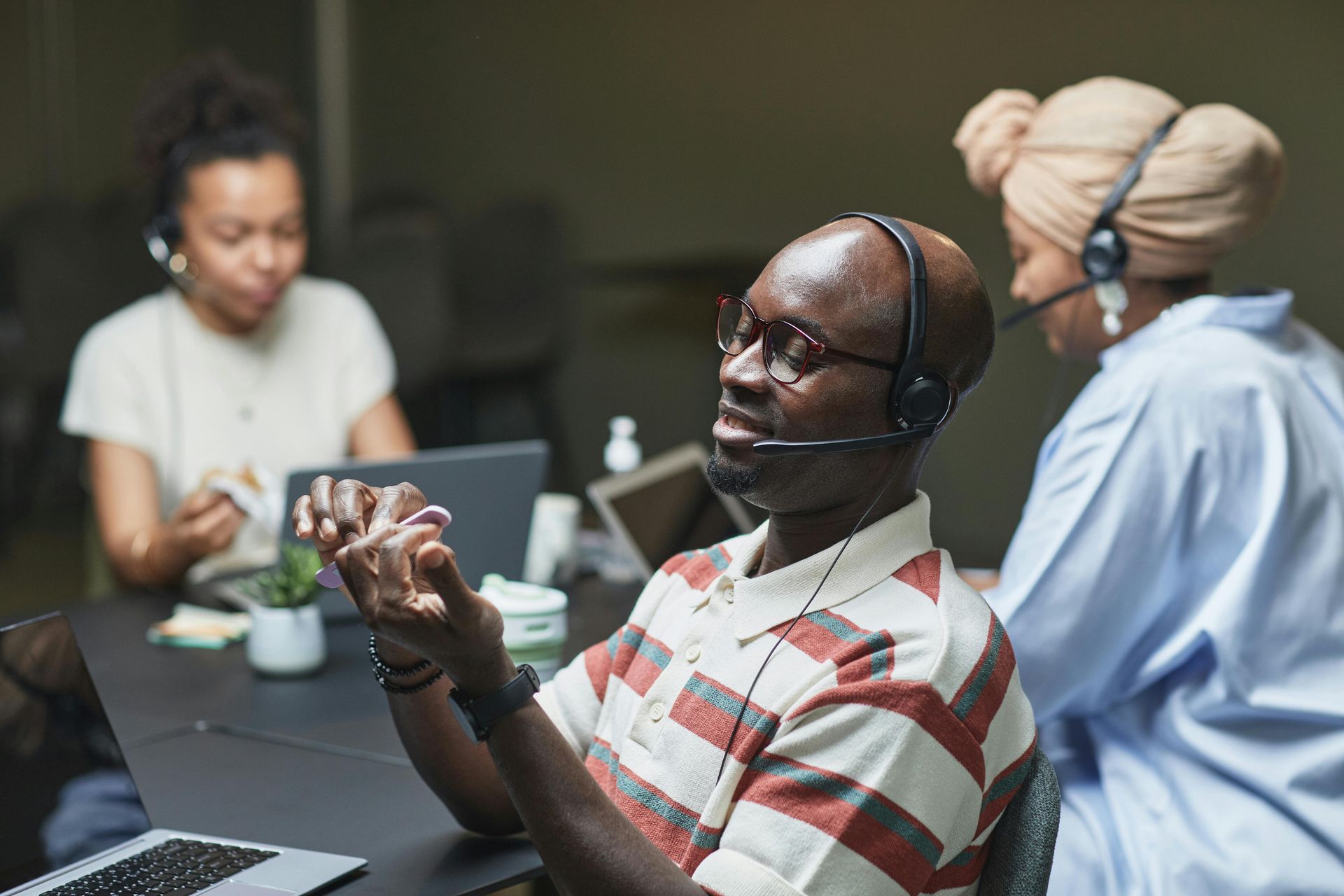 Three people wearing headsets in a video conference meeting, seated at a table with laptops.