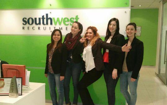 Five people posing in front of a Southwest Records sign in a green office lobby.