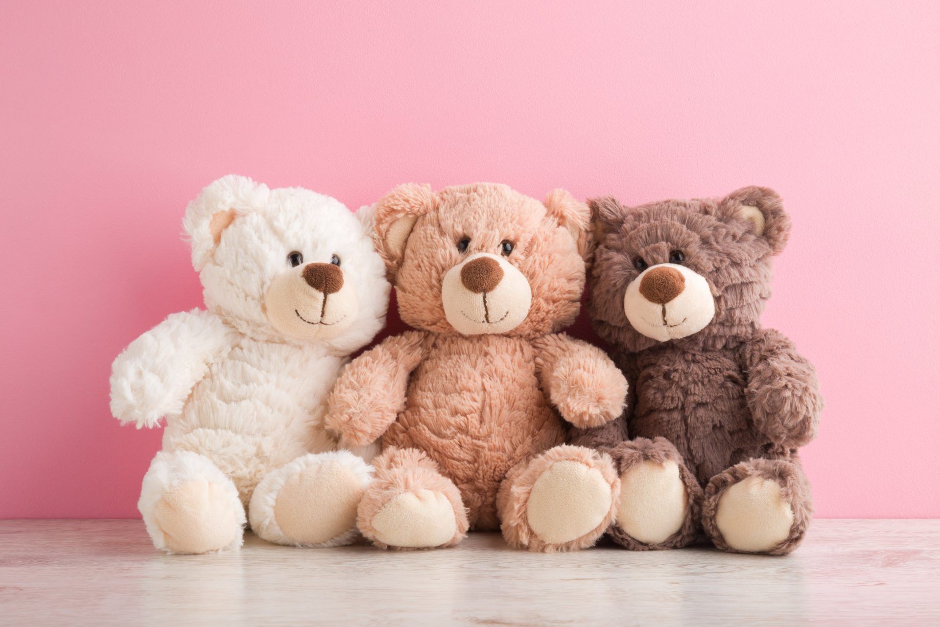 Three teddy bears sitting side by side on a pink background