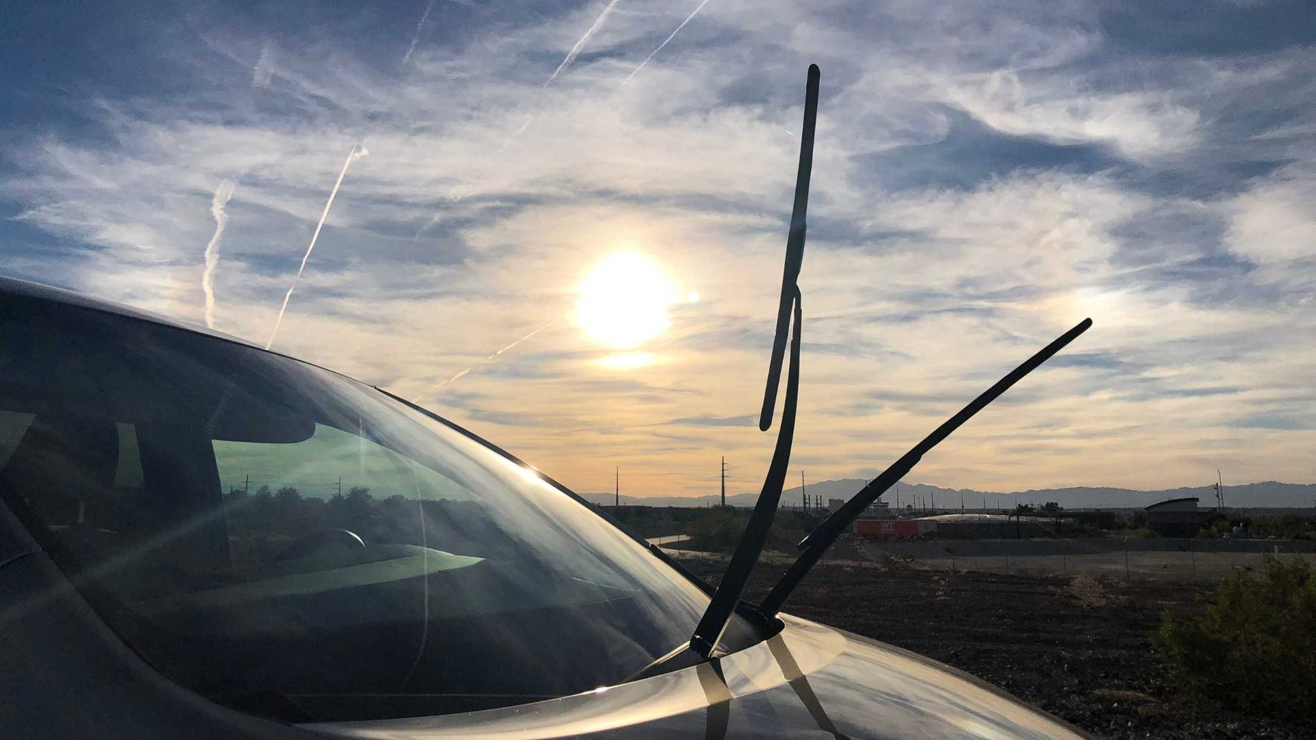 A car with a broken windshield wiper is parked in front of a sunset.