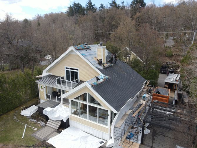 Maison en construction ; ouvriers sur le toit, bardage jaune clair, bardeau gris foncé.
