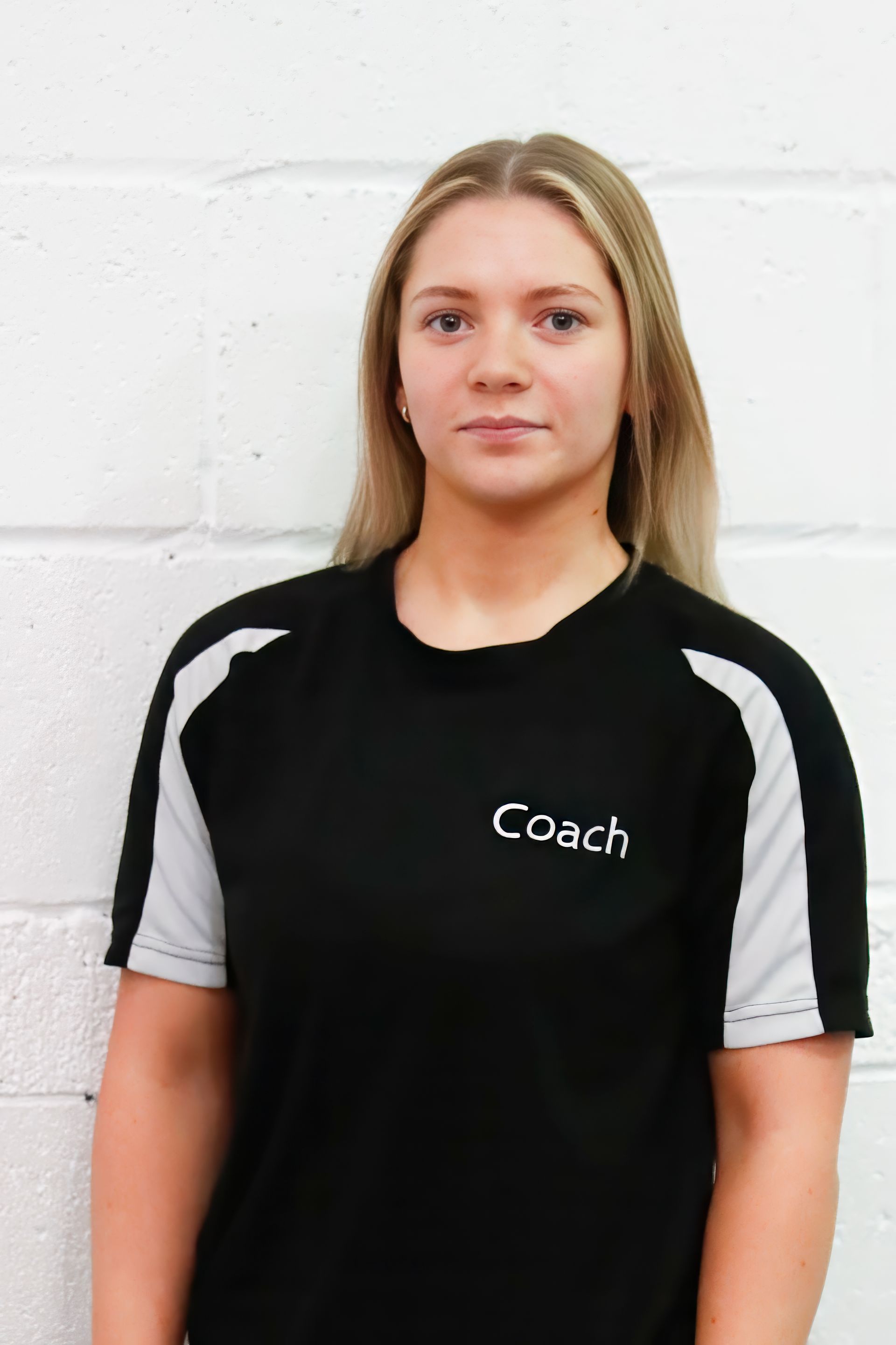 A woman wearing a black coach hoodie stands in front of a white wall