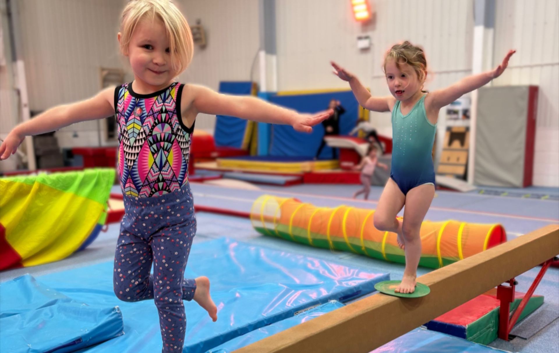 Two little girls are standing on a balance beam in a gym.