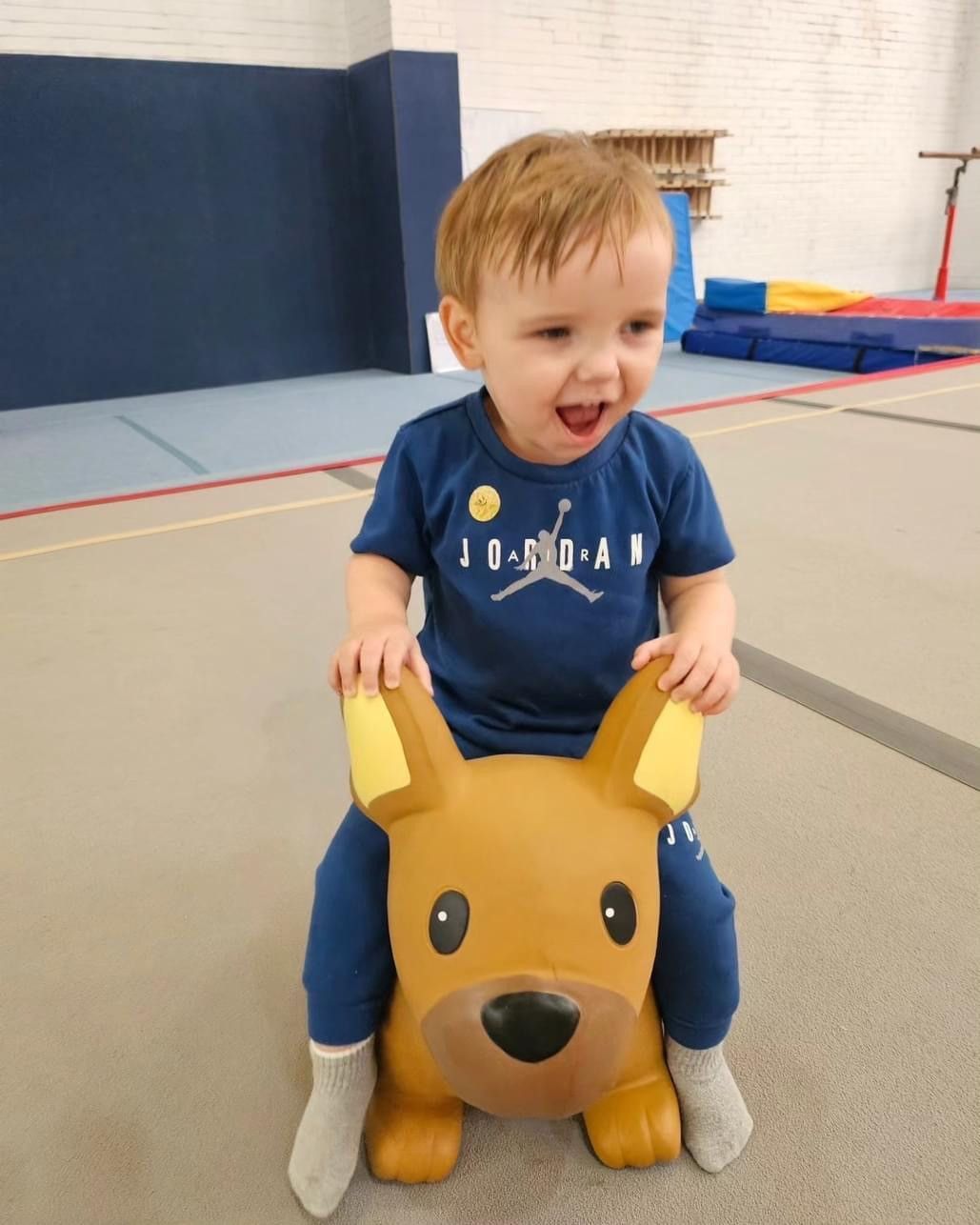 A little boy is sitting on a stuffed animal in a gym