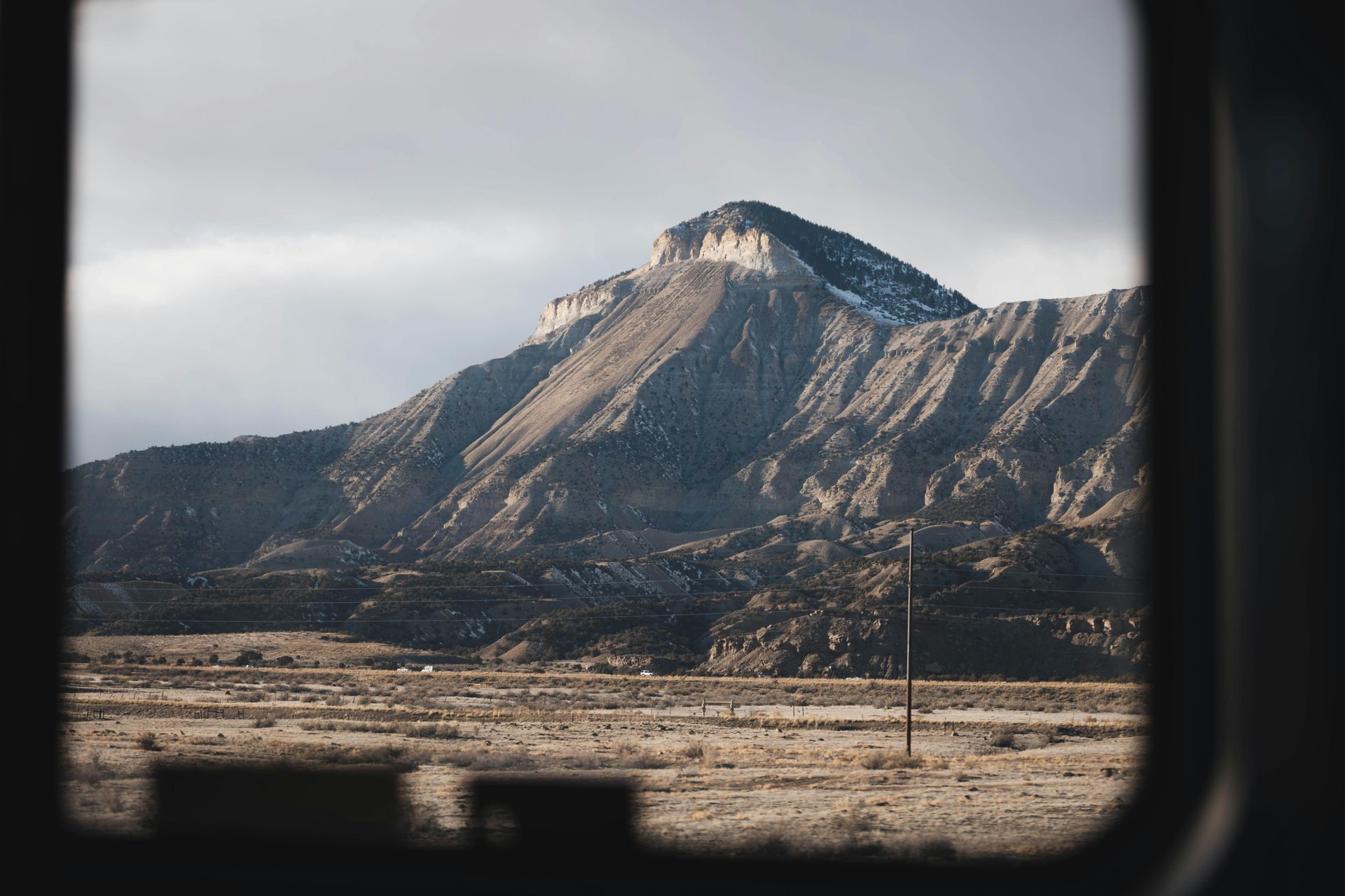 View of a mountain through a rectangular frame. Brown and gray hues. Barren landscape. Cloudy sky.