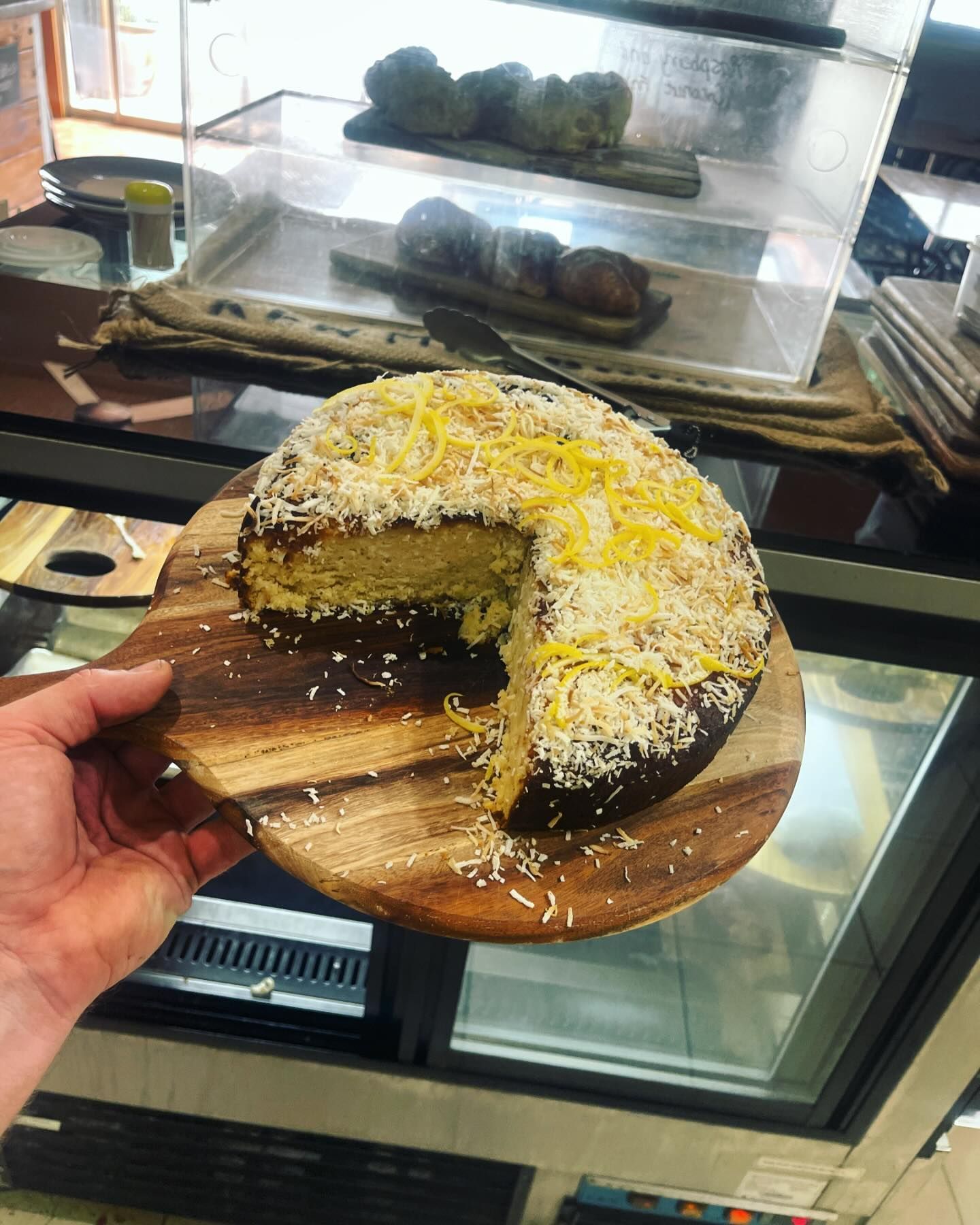 A person is holding a piece of cake on a wooden cutting board.