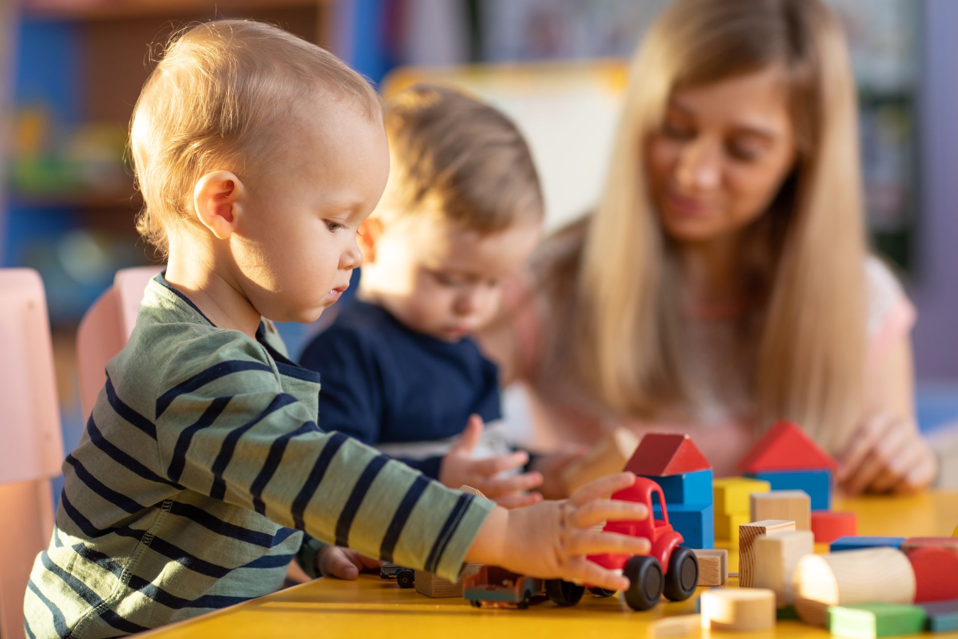 Preschool teacher and cute kids boys playing in kindergarten.
