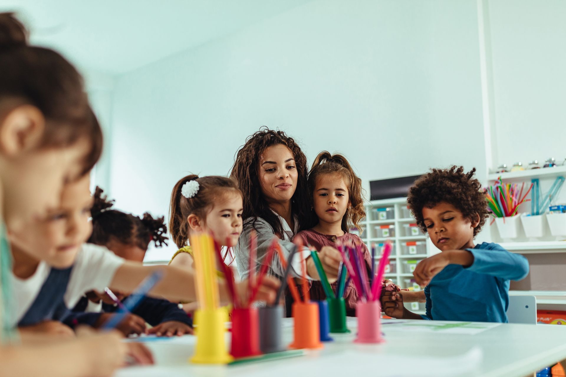 An adult is guiding children using colorful markers and supplies in a learning activity.