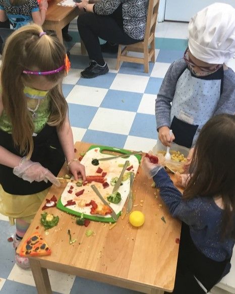 Three children in chef hats and aprons, preparing food on a cutting board at a table.