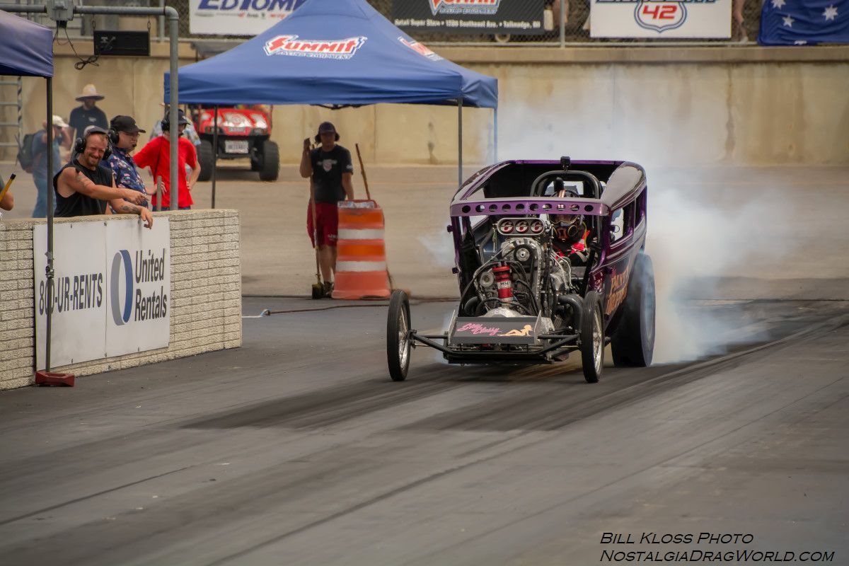A purple dragster is doing a burnout on a race track