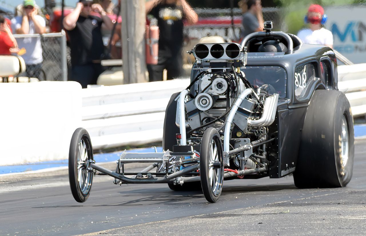 A dragster is driving down a race track with people watching.
