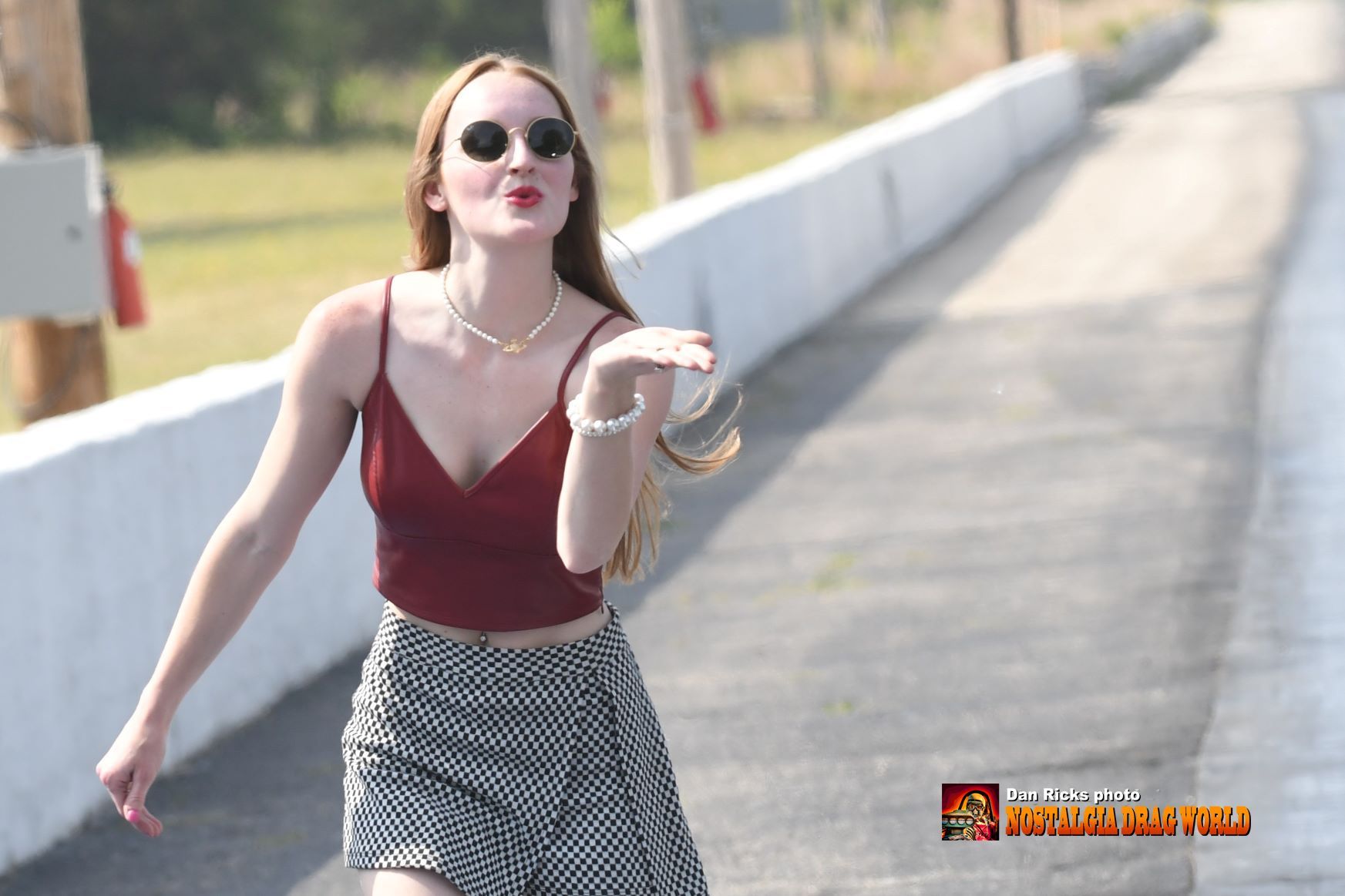 A woman wearing sunglasses and a red top is blowing a kiss