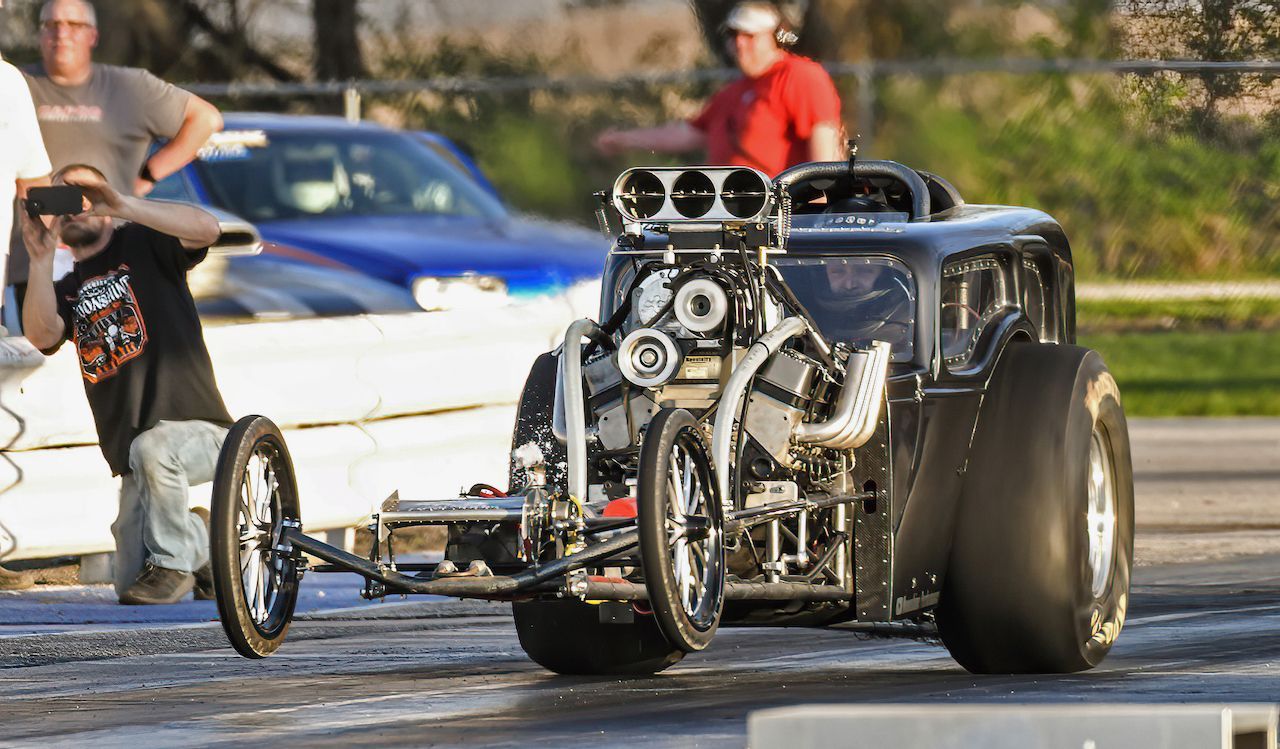 A man is standing next to a drag race car on a track.