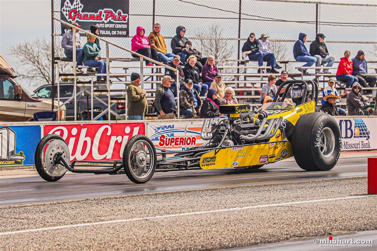 A yellow race car is driving down a track with a sign that says ' rib cri ' on it.