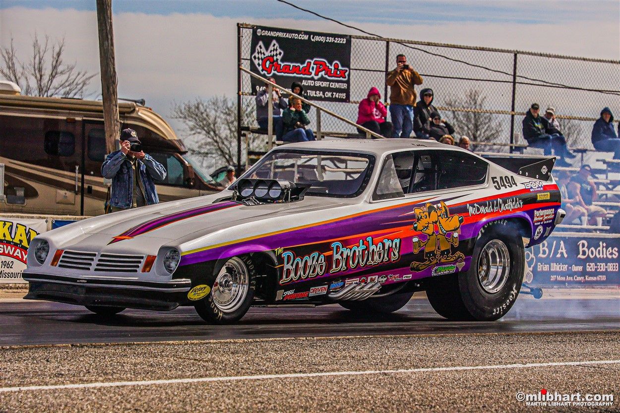 A purple and white drag car is driving down a track.