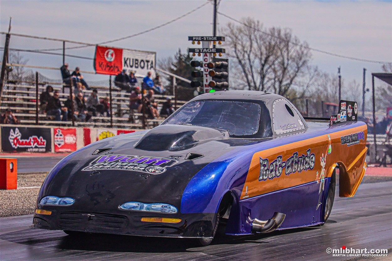 A purple and orange race car is driving down a race track.