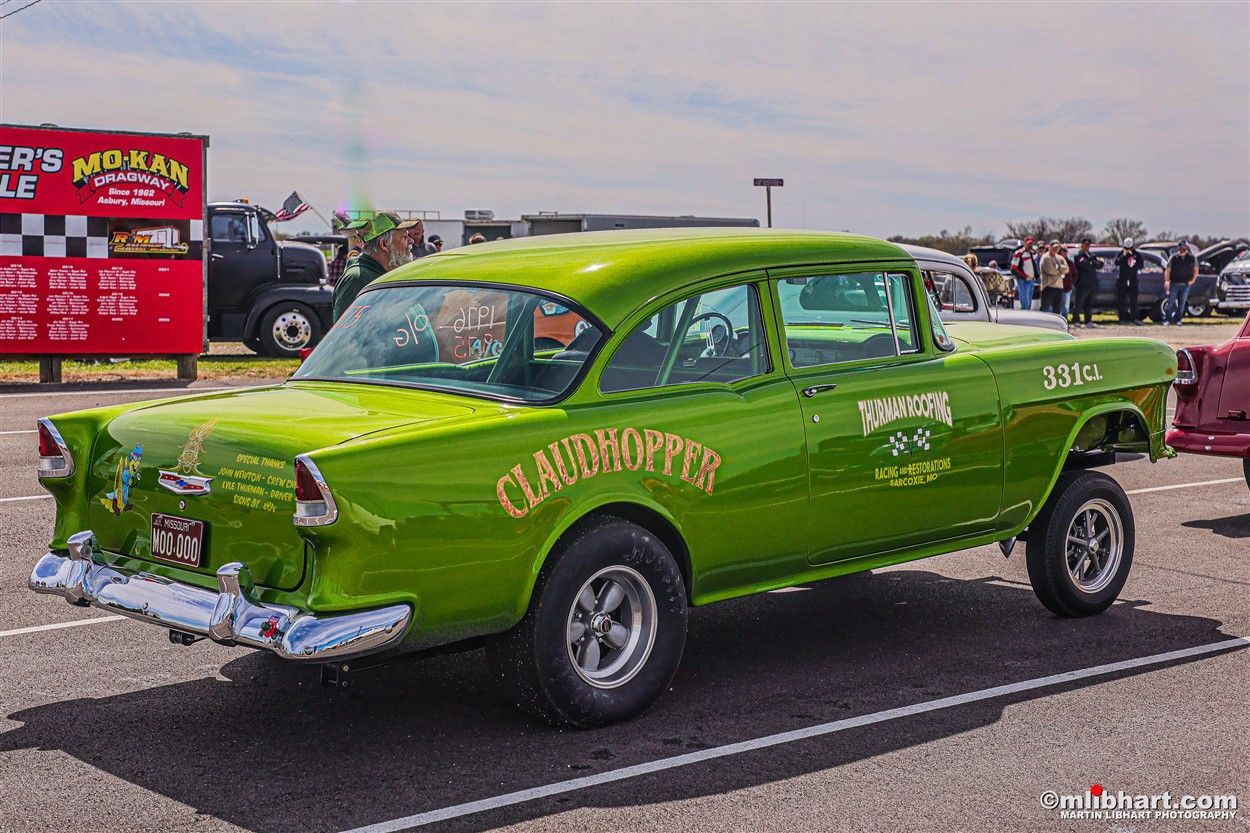 A green car is parked in a parking lot at a car show.